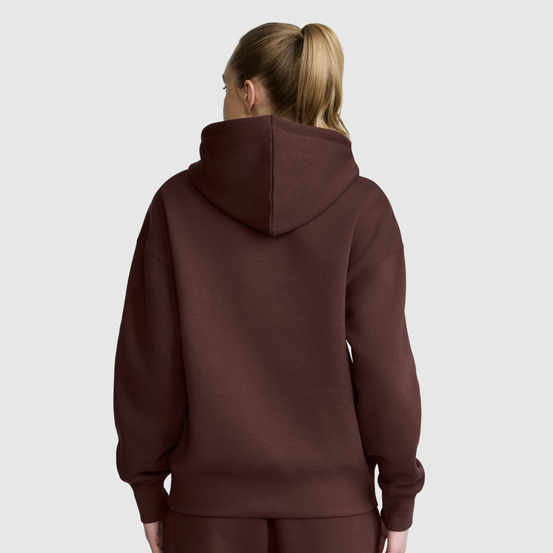 A person with blonde hair in a ponytail is facing away from the camera on a plain light gray background, wearing the Champion Women’s Powerblend Relaxed Hoodie, Script Logo.