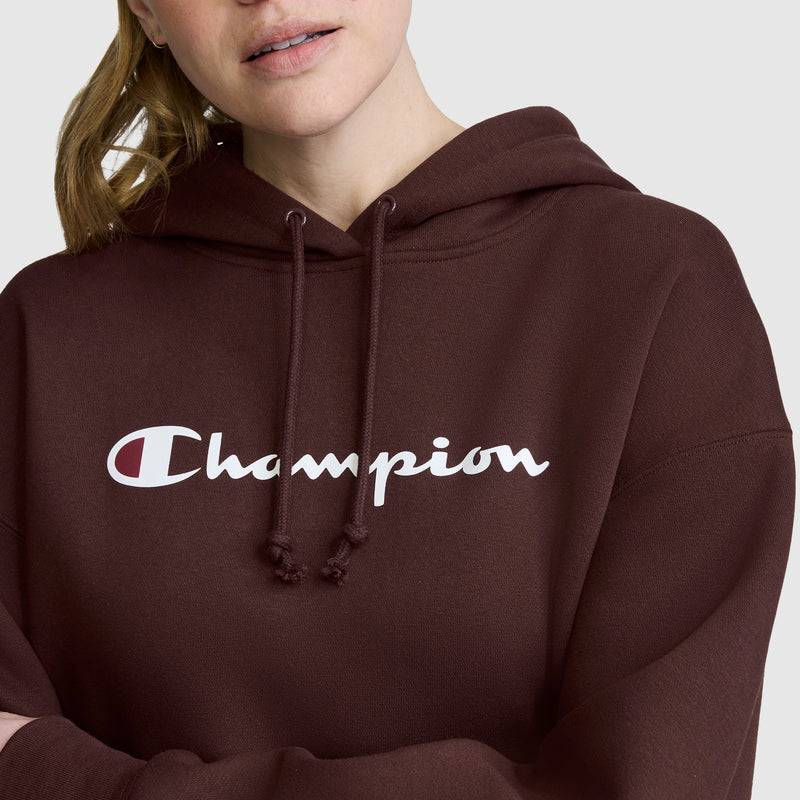 A person wearing a maroon Champion Women’s Powerblend Relaxed Hoodie, Script Logo, with white logo text, is shown from the shoulders up against a plain background. This women’s hoodie from Champion combines cozy Powerblend fleece with relaxed style for maximum comfort.