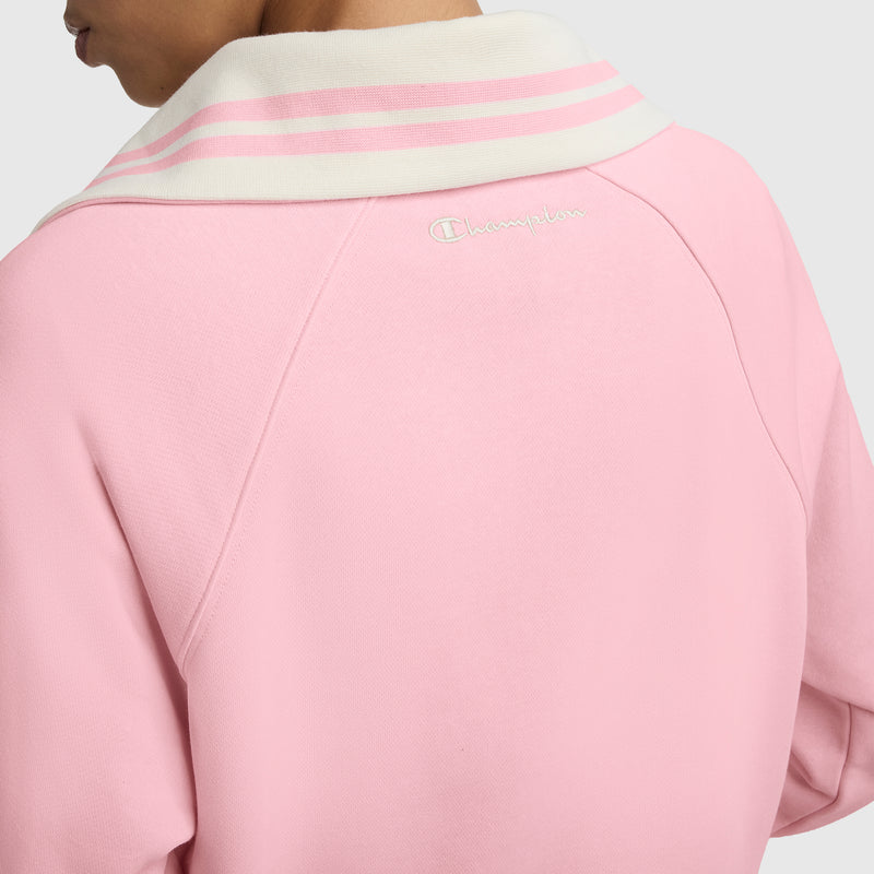 A person is seen from behind wearing the Champion Pitcher Full-Zip Mockneck Top, featuring light pink French terry fabric, a white collar with pink stripes, and an embroidered C logo on the back.