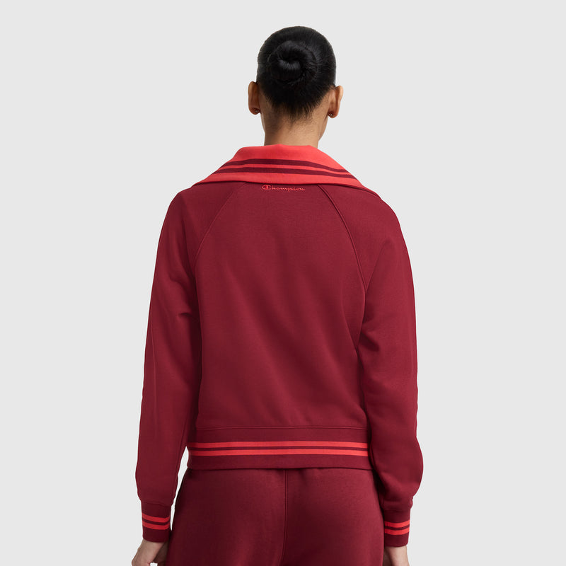 A person with dark hair in a bun is shown from the back, wearing the Champion Pitcher Full-Zip Mockneck Top with C Logo in red, featuring light red trim, against a plain gray background.