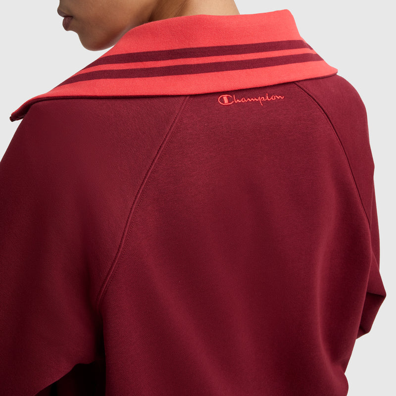 A person wears the Champion Pitcher Full-Zip Mockneck Top featuring a wide red collar with two maroon stripes and "Champion" embroidered near the upper back collar. Only their lower face and shoulders are visible.