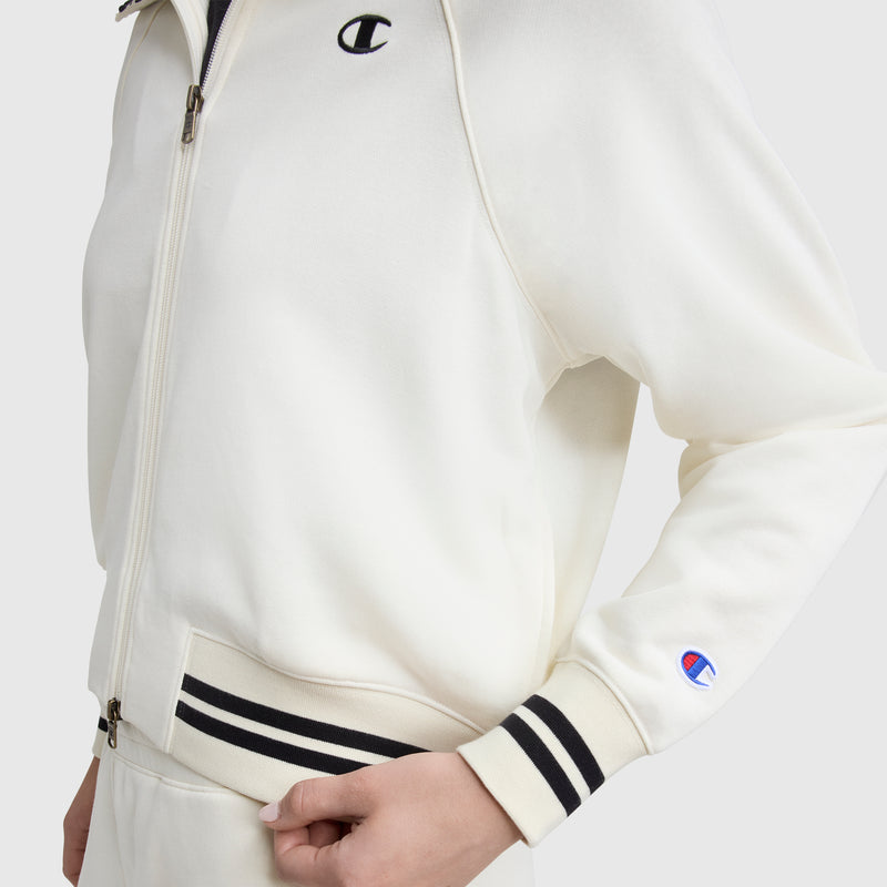 A person wears the Champion Pitcher Full-Zip Mockneck Top featuring black and white striped cuffs and waistband, soft French terry fabric, and C logos on the chest and sleeve. Only their torso and one arm are visible.