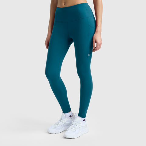 A person is wearing Champion C Logo leggings in teal and white sneakers, standing against a plain light background. The image is cropped from midriff to feet, highlighting the leggings.