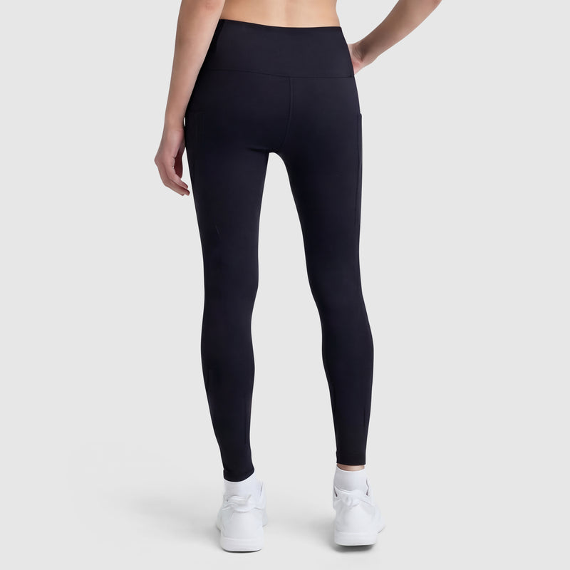 A person wearing Champion C Logo black high-waisted leggings with side pockets and white sneakers stands facing away, one hand on their hip, against a plain light gray background.