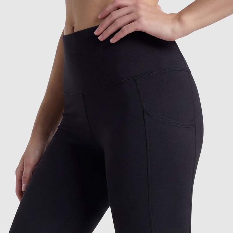 A person wears Champion C Logo high-waisted black leggings with side pockets, made from soft peached fabric, shown waist to mid-thigh against a plain light background, one hand resting on their hip.