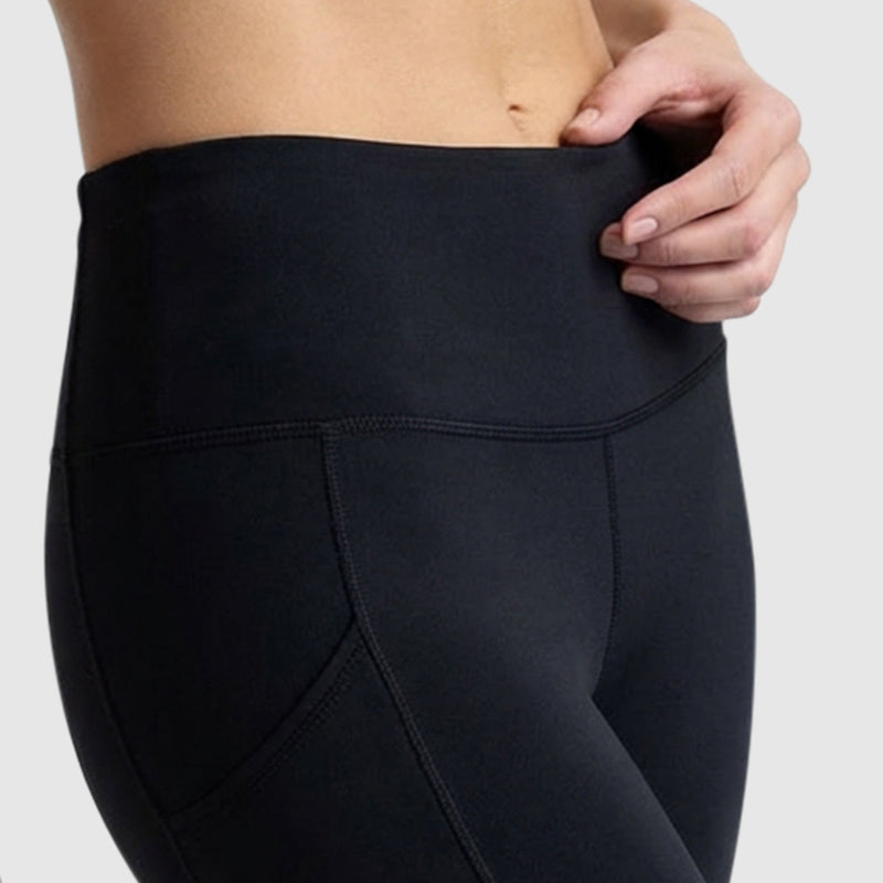 A close-up shows a person wearing Champion Leggings, C Logo in high-waisted black peached fabric, gently pulling at the waistband against a plain light background.