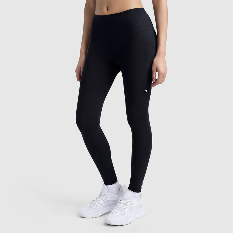 A person models the Champion Leggings, C Logo—high-waisted black leggings with side pockets—paired with white sneakers, against a plain light gray background; only their lower torso and legs are shown.