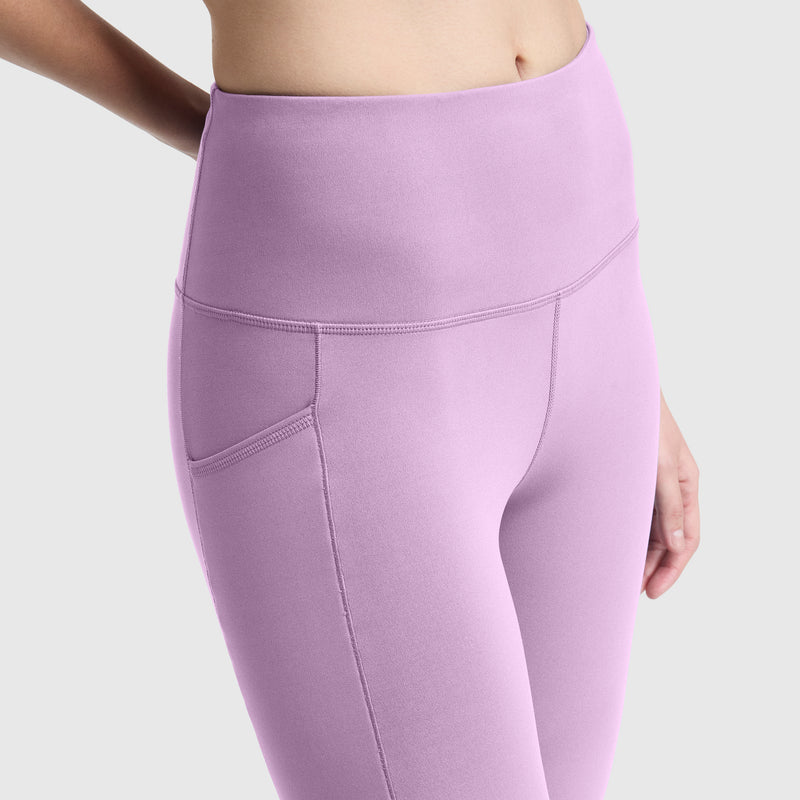 A person is shown from mid-torso to mid-thigh wearing Champion C Logo high-waisted leggings in light purple peached fabric with a side pocket, against a plain light background.