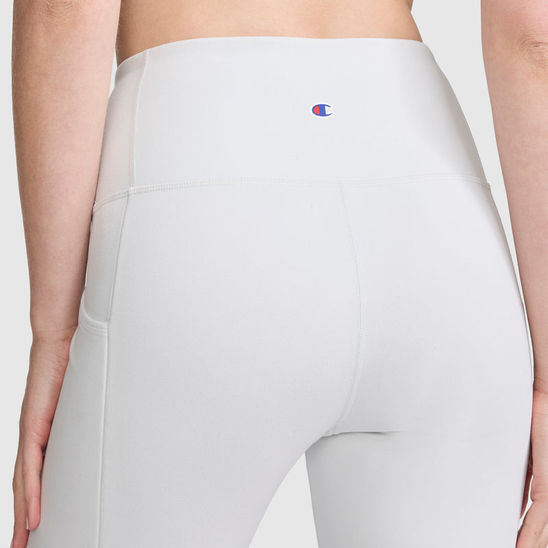A person is shown from the back against a plain background wearing the Champion Leggings, C Logo—high-waisted white athletic leggings featuring the signature Champion logo on the waistband and convenient side pockets.