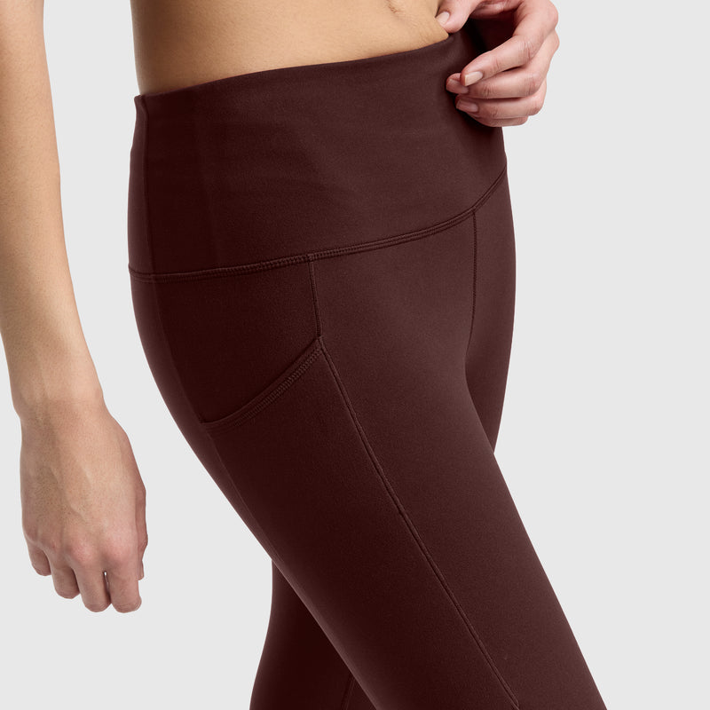 A person wearing high-waisted, dark brown Champion Leggings, C Logo with pockets, shown from mid-torso to thigh against a plain light background.