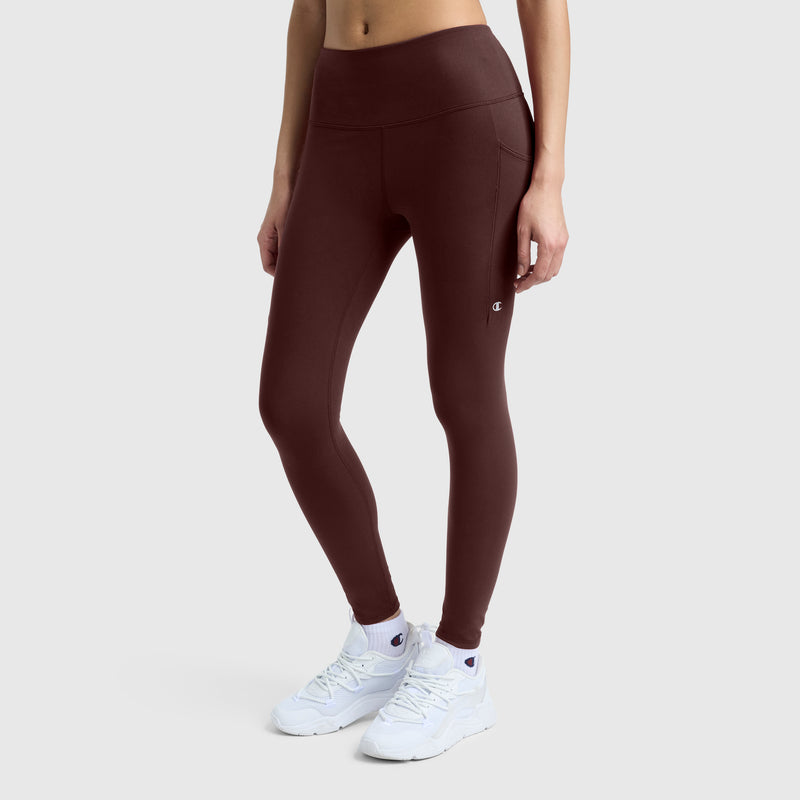 A person wearing Champion’s C Logo high-waisted, silky soft leggings in maroon paired with white sneakers stands against a plain light background, arms relaxed at their sides.