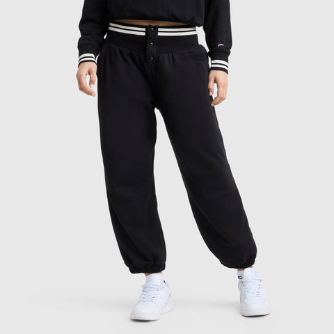 Someone wearing Champion Tackle Snap Front Voluminous Pant in black and a matching black jacket with striped cuffs and waistband, plus white sneakers, stands against a plain light gray background.