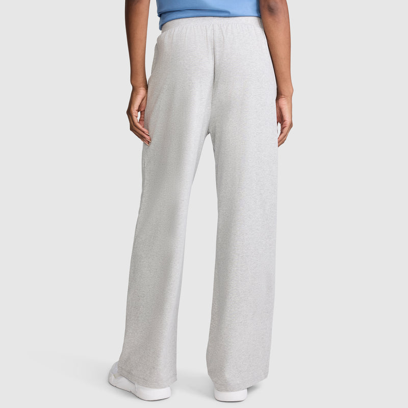 A person is seen from the back wearing Champion Open Bottom Pants in light gray, paired with a light blue top and white shoes.