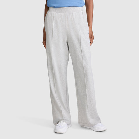 A person dressed in Champion Open Bottom Pant in a loose, light gray stretch jersey, paired with a blue top and white sneakers, stands against a plain background with only the lower half of their body visible.