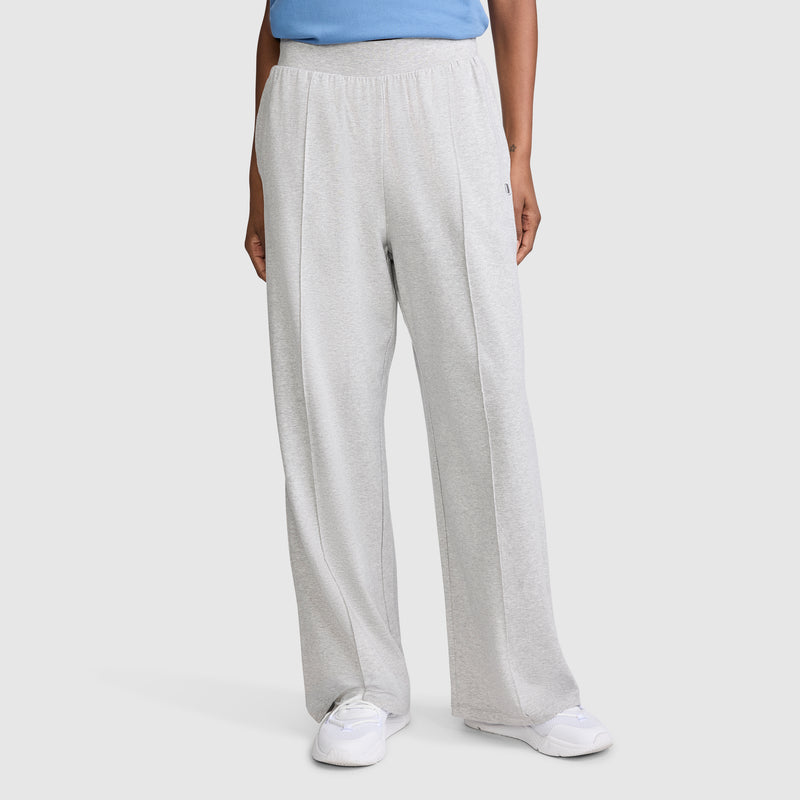 A person dressed in Champion Open Bottom Pant in a loose, light gray stretch jersey, paired with a blue top and white sneakers, stands against a plain background with only the lower half of their body visible.