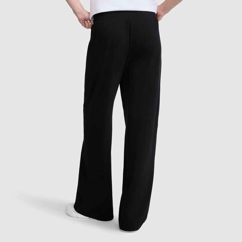 A person wearing Champion Open Bottom Pant in black with white sneakers, shown from the back against a plain light gray background, with only the lower half of their body visible.