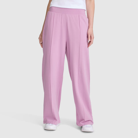 A person wearing Champion Open Bottom Pant in high-waisted pink stretch jersey, paired with a white shirt and white sneakers, stands against a plain light gray background.