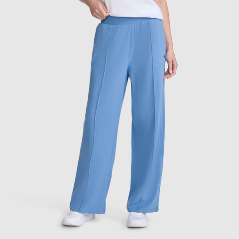 A person wearing Champion’s Open Bottom Pant—loose-fitting, light blue athletic pants made from comfortable stretch jersey with an elastic waistband—paired with white sneakers and a white top, stands against a plain light gray background.