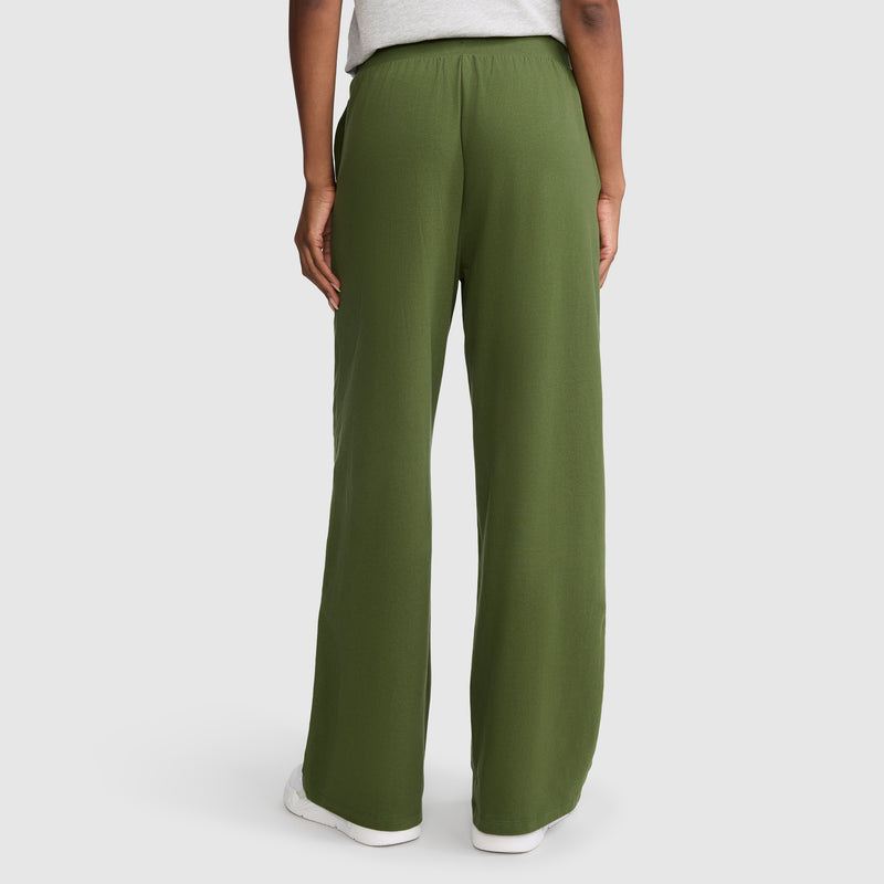 A person stands with their back to the camera against a plain white background, dressed in loose-fitting olive green Champion Open Bottom Pants and a light gray top.