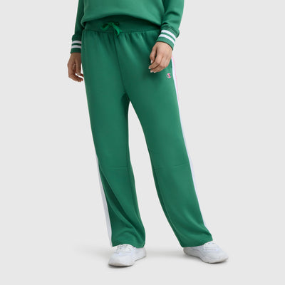 Model wears Champion Tennis Court Wide Leg Pant, C Logo, in green soft scuba fabric with white side stripes, paired with a matching green sweatshirt and white sneakers. The athletic heritage is highlighted by the iconic Champion logo.