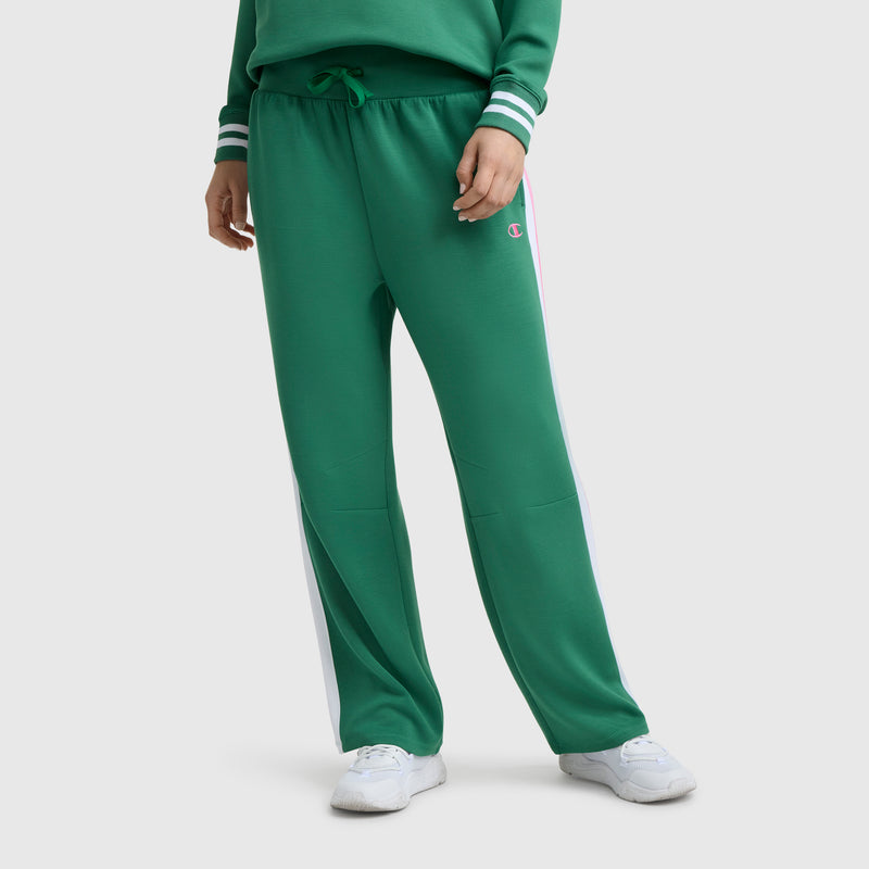 Model wears Champion Tennis Court Wide Leg Pant, C Logo, in green soft scuba fabric with white side stripes, paired with a matching green sweatshirt and white sneakers. The athletic heritage is highlighted by the iconic Champion logo.