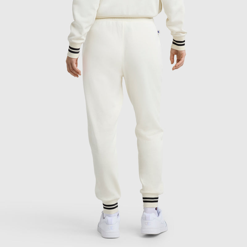 A person is seen from the back in Champion Pitcher Pant, C Logo joggers with black-and-white striped cuffs and white sneakers, set against a plain background for a sport-luxe style.