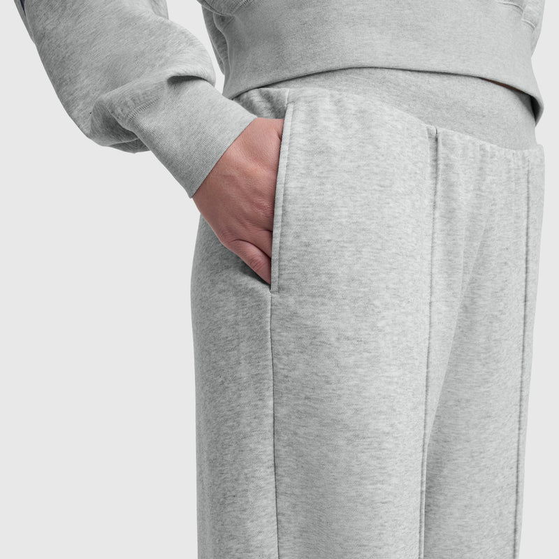 A person wearing Champion Tackle Open Bottom Pant, C Logo in light gray stands with their right hand in the pocket, shown from waist to mid-thigh against a plain background.