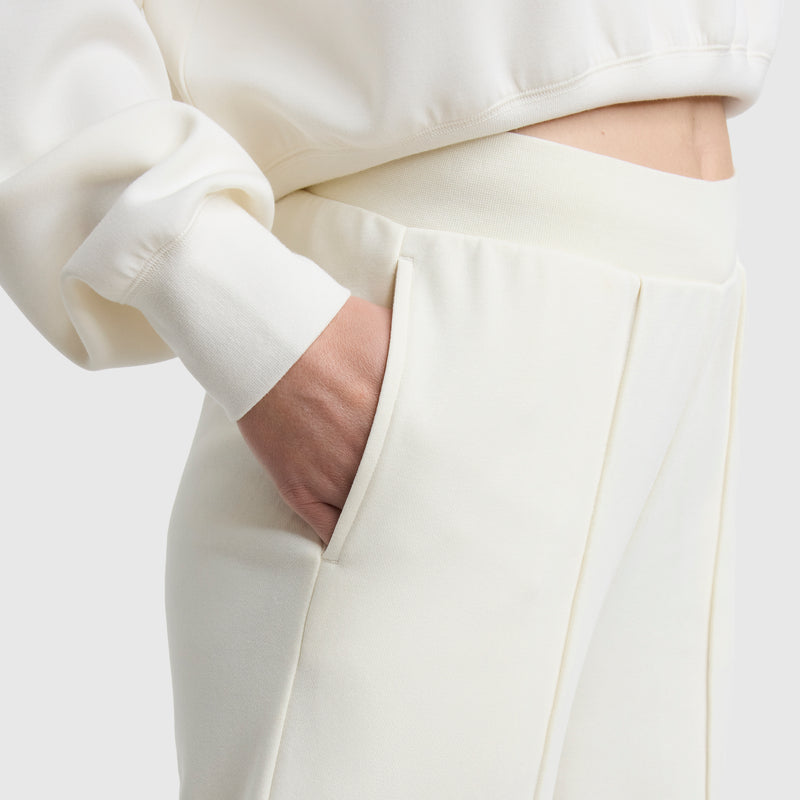 A person wearing Champion’s Tackle Open Bottom Pant with C Logo, featuring a relaxed fit, high waist, and soft off-white French terry fabric, hand in pocket to highlight the cozy material and matching style.