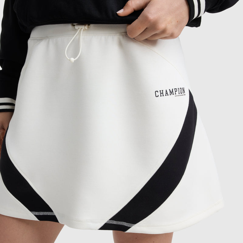 A person wears the Champion Endzone Color Block Skirt, white with black diagonal stripes and a drawstring waistband. Only their lower torso and one hand on their hip are shown.
