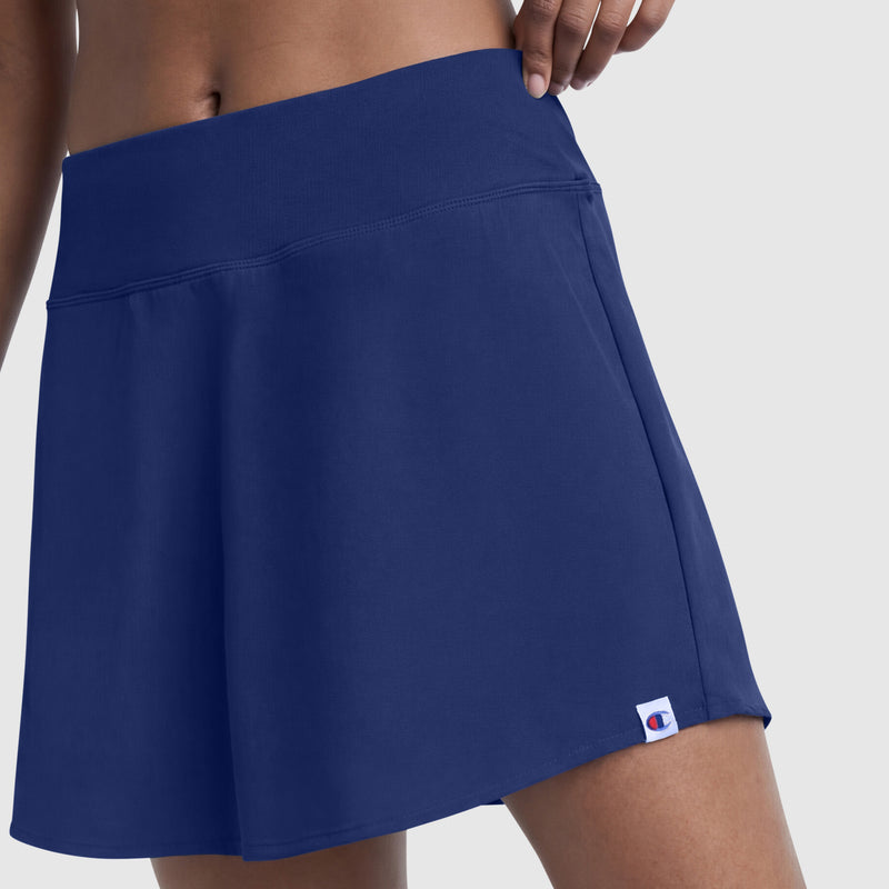 A close-up of a person wearing the Champion Courtside Skort, featuring sporty style and a small C logo patch near the bottom hem, set against a plain light background.