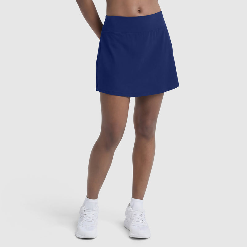 A person stands against a plain background, showcasing the lower half of their body in a Champion Courtside Skort with C Logo, paired with white socks and sneakers—highlighting effortless court style.