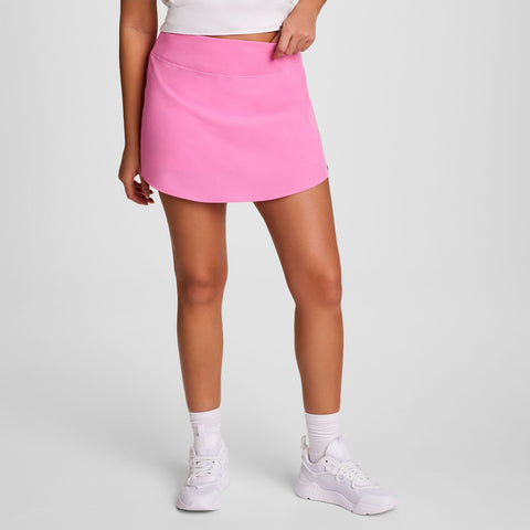 A person in a white crop top, white socks, white sneakers, and the Champion Courtside Skort with C Logo poses against a plain light background. Their face is not visible in the image.