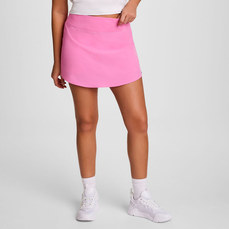 A person in a white crop top, white socks, white sneakers, and the Champion Courtside Skort with C Logo poses against a plain light background. Their face is not visible in the image.