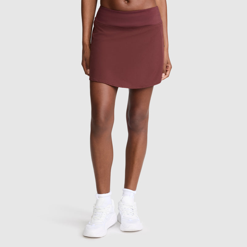 A person stands against a plain background wearing the Champion Courtside Skort, C Logo, paired with white socks and white sneakers. Channeling effortless court style, their arms are relaxed by their sides, and their head is not visible in the image.