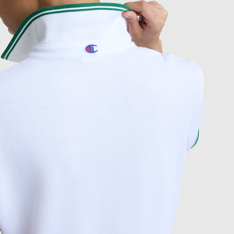 A person adjusts the collar of the Off The Court Polo Dress with green trim, showcasing Champion’s embroidered C logo on the back. The image is cropped to display only the upper back and part of one arm.