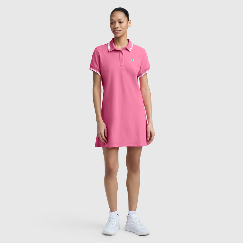 A woman models the Champion Off The Court Polo Dress with C Logo against a plain background, styling it with white socks, sneakers, and a tied-back hairstyle for a relaxed, retro-inspired look.