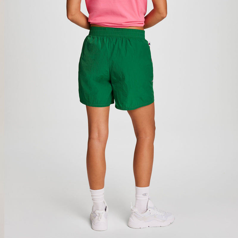 Person stands with their back to the camera in a pink shirt, Champion 5" Courtside Short with C Logo (green), white crew socks, and white sneakers against a plain white background.