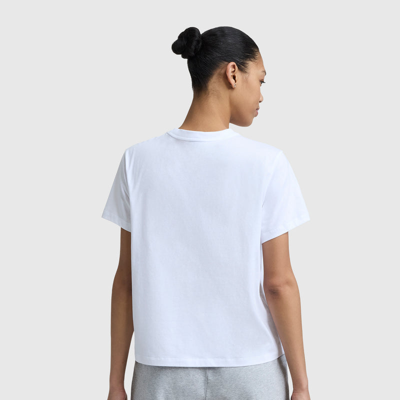 A person with dark hair in a bun is seen from behind, wearing the Champion Cherry On Top Graphic T-Shirt and light gray pants, standing against a light gray background.