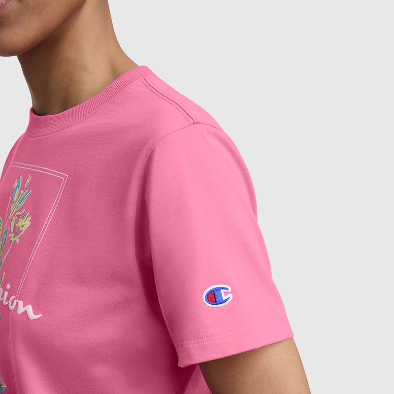 Someone wearing Champion's Painted Bouquet Graphic T-Shirt with a floral chest graphic and C logo patch on the left sleeve, shown from the shoulders up against a plain background.
