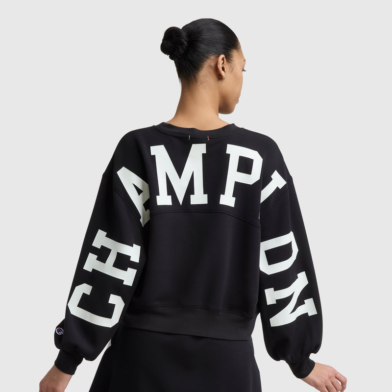 A person with hair in a bun is seen from behind wearing a black Champion Endzone Loose Fit Crewneck, featuring the bold C Logo on the back and sleeves for an athletic, standout look.