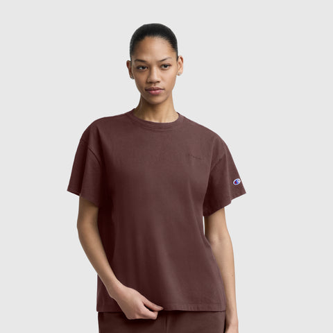 A woman wears the Champion Short Sleeve Loose Fit T-Shirt in maroon, paired with matching pants, as she stands against a plain gray background and looks directly at the camera with a neutral expression.