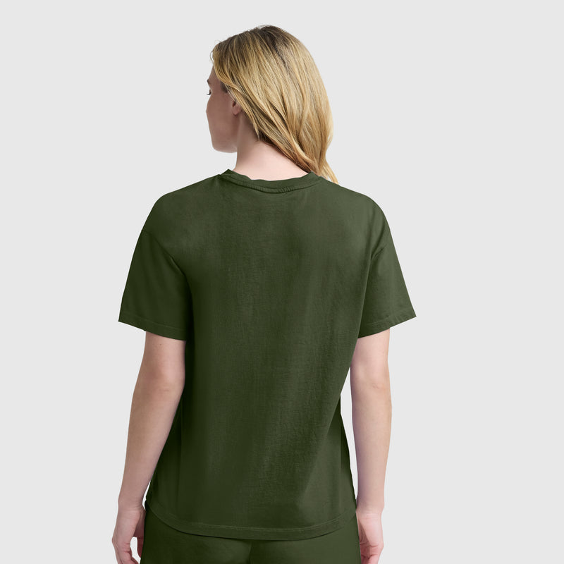 A person with long blonde hair is shown from the back, standing against a light gray background and wearing a plain dark green Champion Short Sleeve Loose Fit T-Shirt and pants.