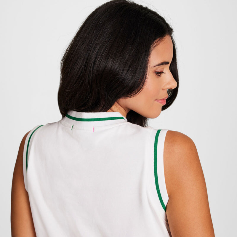 A woman with long dark hair, facing away, wears the Champion Country Club Sleeveless Top with embroidered script logo in white French terry and green trim. She glances over her shoulder with a neutral expression against a plain light background.
