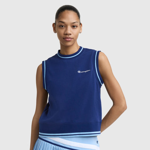 A woman wears a navy blue Champion Country Club Sleeveless Top with an embroidered script logo and light blue trim, paired with a matching pleated skirt, standing against a plain light gray background.