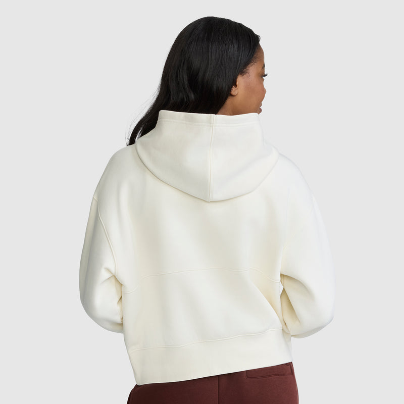 A person with long dark hair is seen from behind, wearing a Champion Training Half-Zip Fleece Hoodie in white and maroon pants, standing against a plain light background.