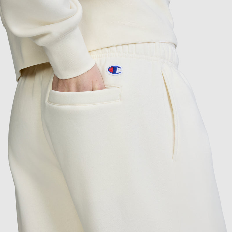 A person wearing the Champion Fleece Cargo Training Pant in cream, with a hand in the side pocket, displays the blue and red Champion logo near the waistband against a plain background.