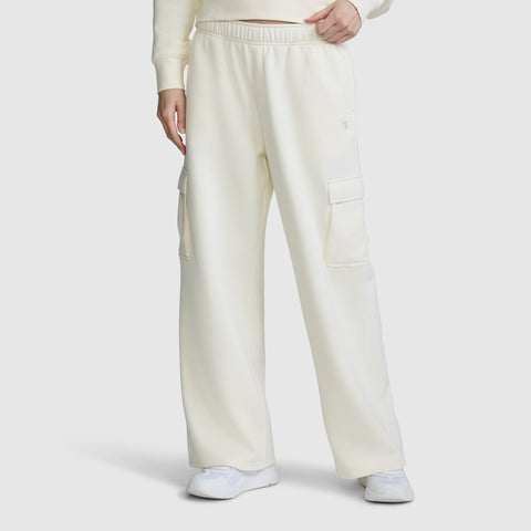 A person is wearing the Champion Fleece Cargo Training Pant for women in a loose, off-white fit with side pockets, styled with a coordinating sweatshirt and white sneakers, standing against a plain white background.