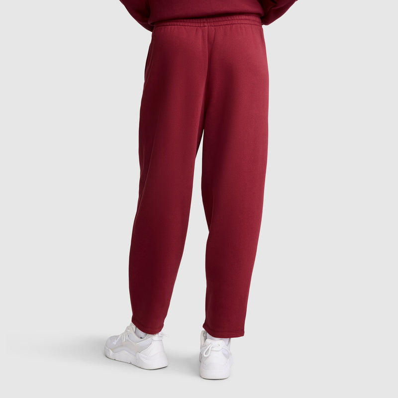 A person is shown from the back, standing on a plain light gray background, wearing Champion Barrel Leg Fleece Pants in maroon and white sneakers.