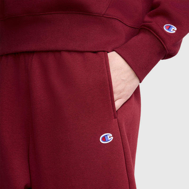 A person wearing matching maroon Champion sweatshirt and Barrel Leg Fleece Pant, with a hand in the pocket. Both garments display the Champion logo, and the pants are styled for a trendy, relaxed fit.