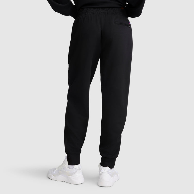 A person is seen from the back, standing against a plain light gray background, wearing the Champion Taper Leg Jogger with Zippers in black paired with white sneakers.